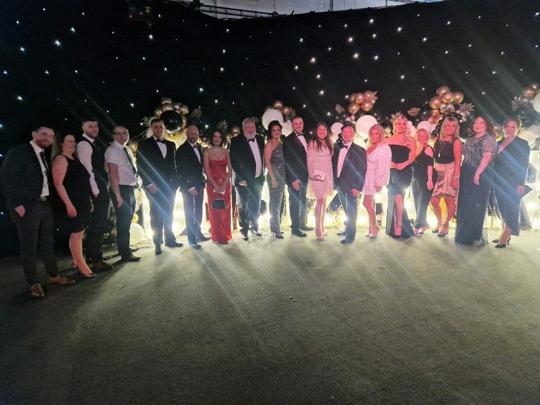 A team from Polypipe Building Products dressed in black tie stand in front of a giant #DNBizAwards sign at the 2022 Doncaster Business Awards.