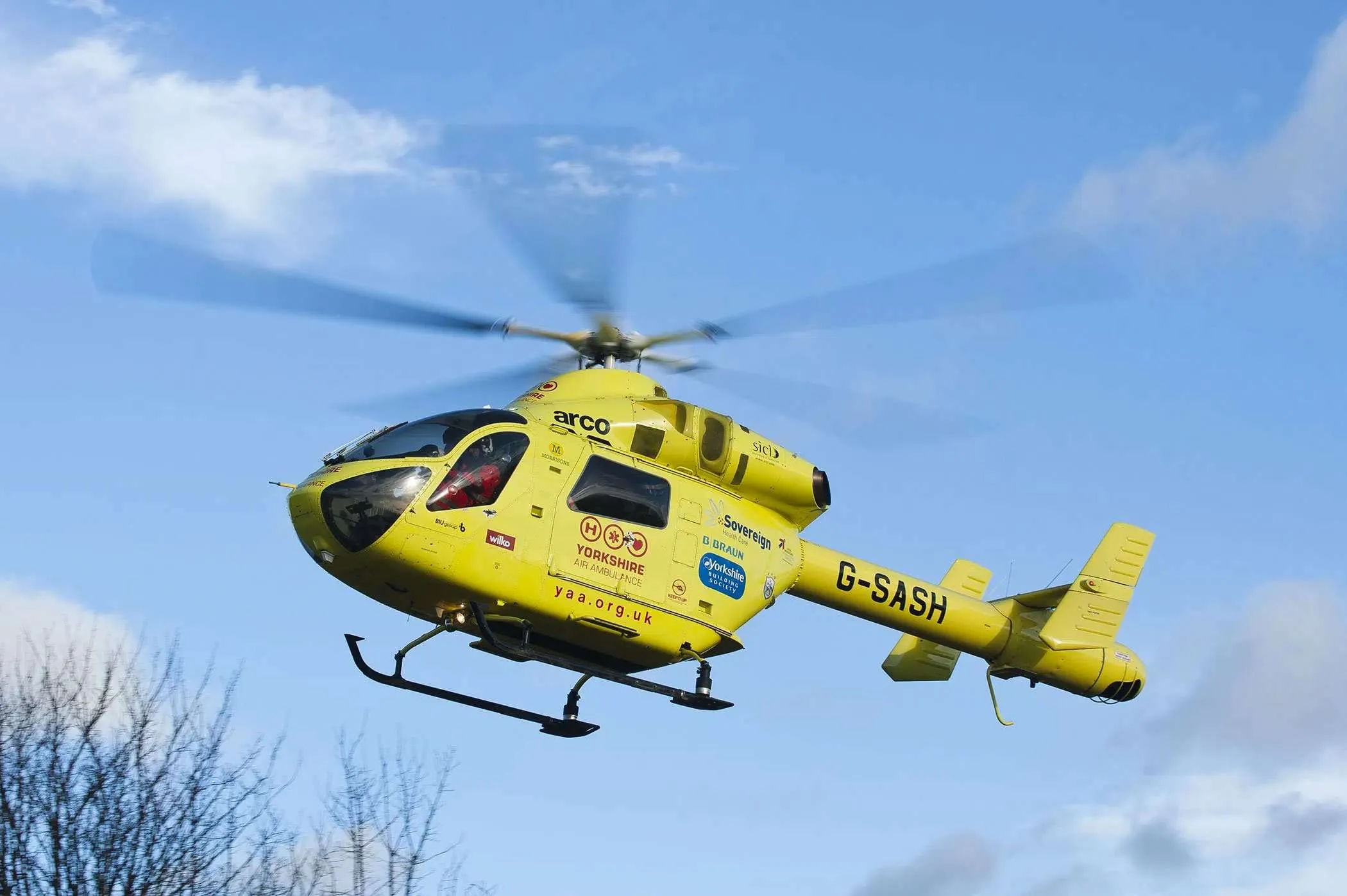 Yorkshire Air Ambulance, a yellow helicopter, in flight.
