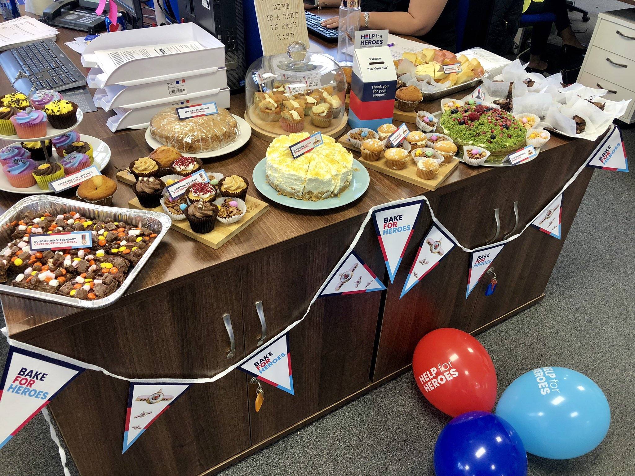 A table containing lots of baked goods decorated with Help for Heroes banners, bunting and signage