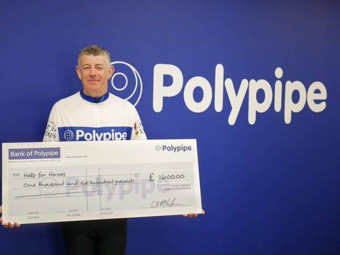 Regional Sales Manager Gary Foord stands holding an oversized cheque for £1600 for monies raised during a charity cycling challenge.